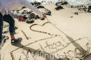 Ein Sprachschüler schreibt "Ich liebe dich Maltalingua" in den Sand