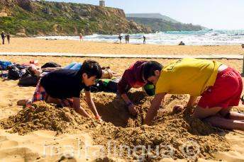Gruppenleiter und Sprachschüler graben ein Loch am Strand