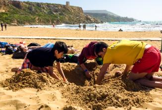 Gruppenleiter und Sprachschüler graben ein Loch am Strand